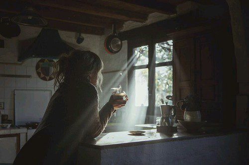 Person enjoying coffee in sunlit kitchen